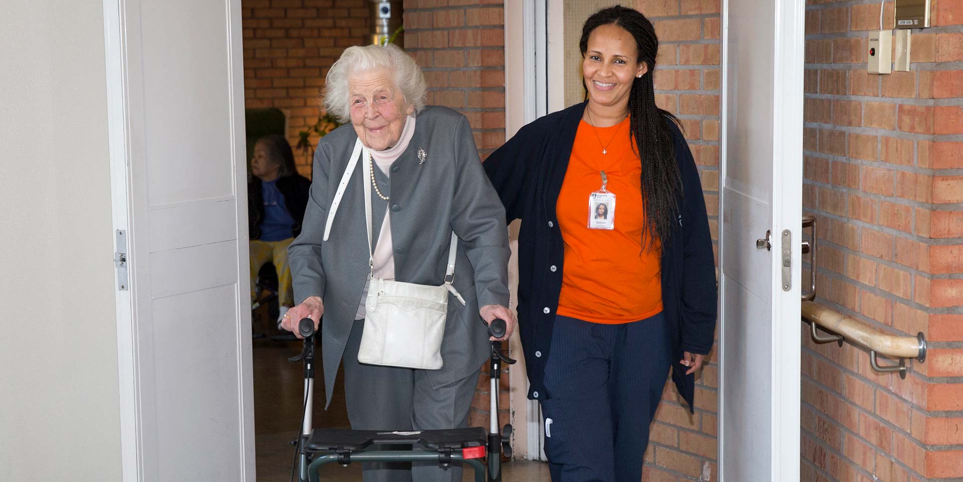Äldre kvinna med rullator och personal från äldreomsorgen