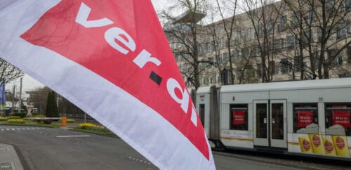 En flagga från fackförbundet Verdi vajar framför en spårvagn med texten "varningsstrejk" klistrad på rutorna