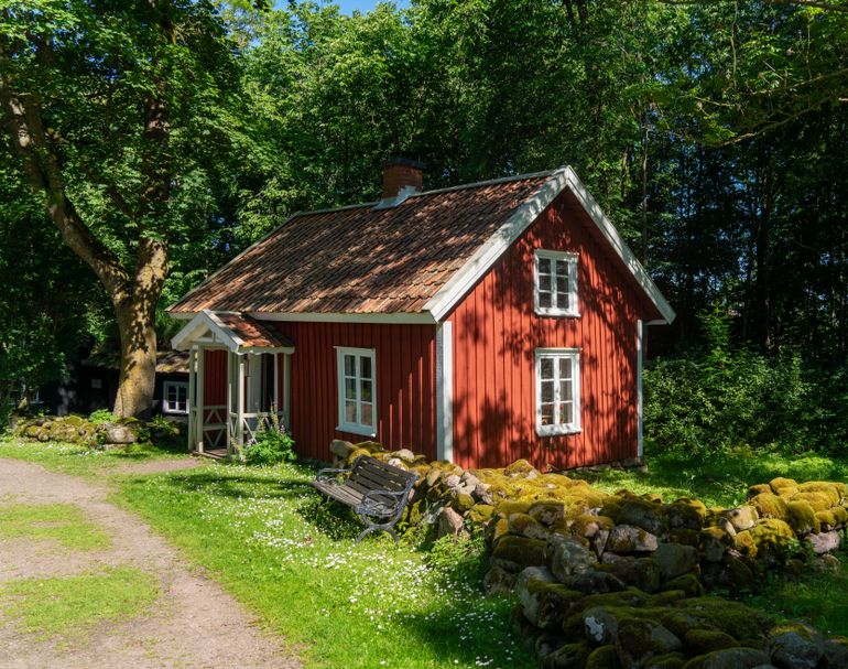 Quaint red cottage surrounded by lush greenery in Falköping, Sweden.